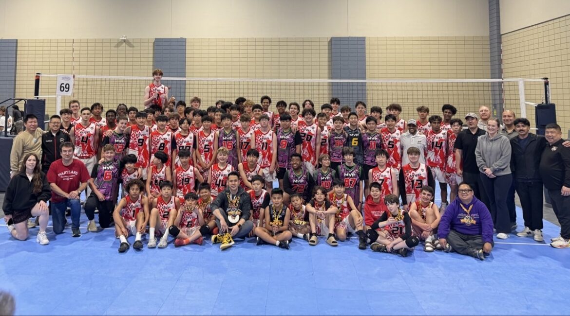 MVP Boys volleyball team and coaches posing together in three rows after a tournament — back row standing, middle row kneeling, front row seated with trophy. Players wear pink, purple, red, and dark MVP jerseys with visible numbers.