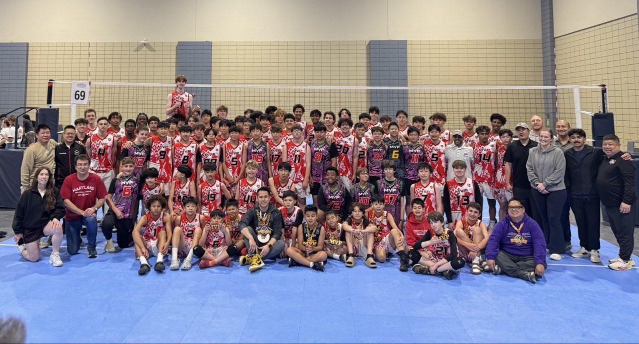 MVP Boys volleyball team and coaches posing together in three rows after a tournament — back row standing, middle row kneeling, front row seated with trophy. Players wear pink, purple, red, and dark MVP jerseys with visible numbers.